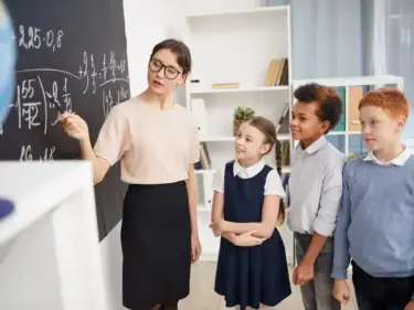 eine Lehrerin zeigt drei Schülern etwas an der Tafel